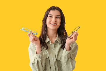 Happy smiling young woman holding eyeglasses on yellow background
