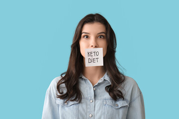 Surprised young woman with sticky note on mouth against blue background. Keto diet concept