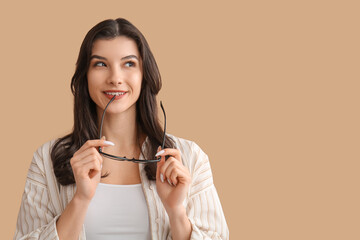 Happy smiling young woman holding eyeglasses on beige background