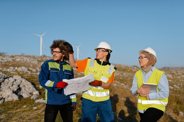 A team of engineers and workers oversees a wind turbine project at a modern wind farm, working...