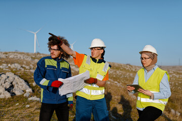 A team of engineers and workers oversees a wind turbine project at a modern wind farm, working...