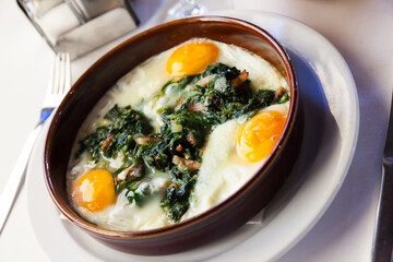 Delicious fried eggs with spinach, ham and raisins in clayware. Traditional Catalan dish..