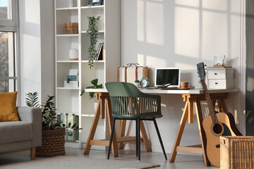 Interior of stylish office with workplace, shelving unit, guitar and laptop
