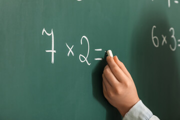 Girl writing on chalkboard during lesson in classroom, closeup