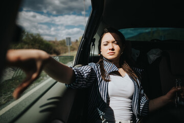 A young female passenger relaxes by extending her arm out of the car window while basking in the sunlight on a road trip.