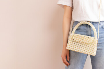 Woman with a handicraft bag made from pearl imitation beads in front of beige background. Place for...
