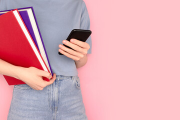 Woman holding books in her hands and use smartphone in front of pink background. Place for text.