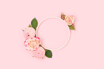 Round frame made of green leaves and rose flowers on a pink background. Floral composition with place for text.