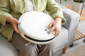 Senior woman with robot vacuum cleaner sitting on sofa at home