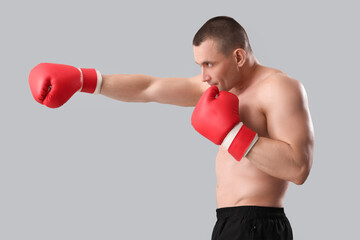 Muscular male bodybuilder in boxing gloves on grey background