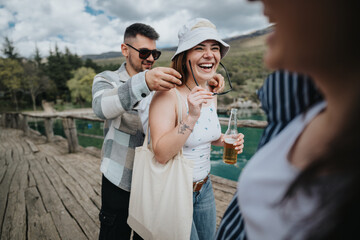 Group of happy friends laughing and sharing drinks on a wooden pier by a lake, a joyful moment on their travel adventure.