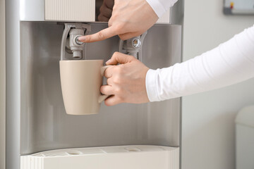 Female hands filling cup with filtered water from cooler in room