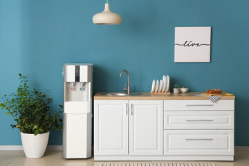 Interior of stylish kitchen with modern water cooler near blue wall