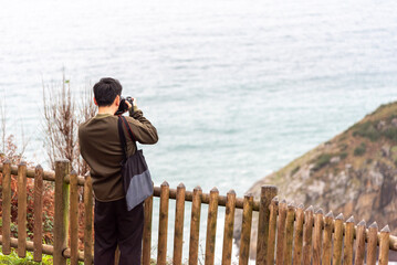 Close-up shot of a Japanese tourist with his back to a professional camera taking a picture of the...