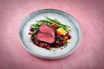 Badkamer foto achterwand Traditionally roasted saddle of venison fillet with spätzle, vegetable and fruits in chocolate red wine sauce served as close-up on a Nordic design plate with copy space © HLPhoto