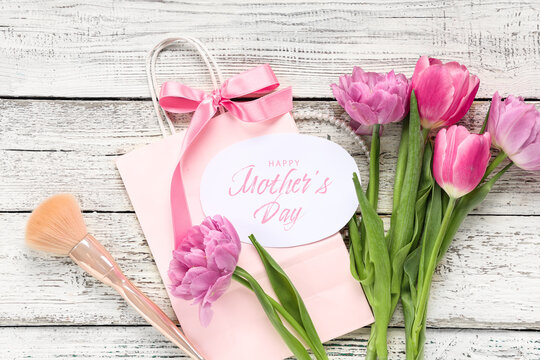 Greeting card with text HAPPY MOTHER'S DAY, beautiful tulips and makeup brush on white wooden background