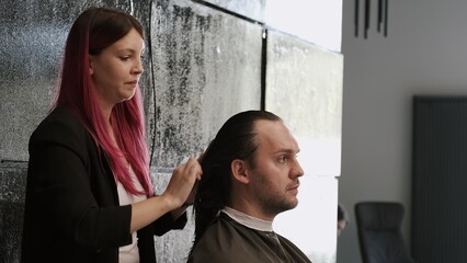 Hair stylist combing a man's long hair in a modern salon
