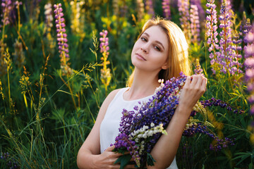 A beautiful blonde in a white dress with a bouquet of wildflowers. Bouquet of lupine