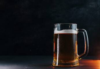 Light cold beer mug with water drops on a black table , backlight