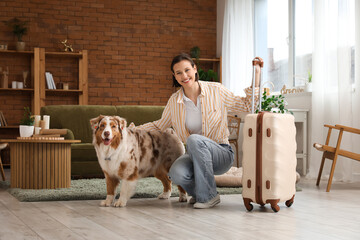 Pretty young woman with suitcase and cute Australian Shepherd dog at home