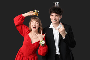 Happy couple dressed for prom with crowns showing "devil horns" gesture on black background © Pixel-Shot