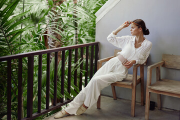 Smiling woman enjoying a tropical vacation on a sunny balcony She stands in a trendy outfit,...