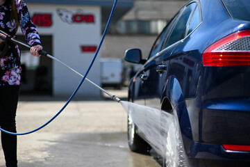 a woman washes a car at a car wash. She holds a water pressure gun in her hand