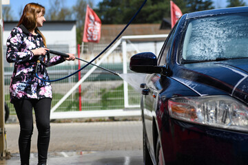a woman washes a car at a car wash. She holds a water pressure gun in her hand