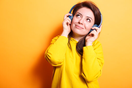 Smiling woman in casual clothing wearing wireless headphones and listening to music. Image of caucasian female adult with headset looking upwards, enjoying relaxing sounds and songs.
