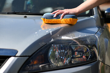 A young woman washes the car using an orange-gray sponge. a detailed view of the lights and a...