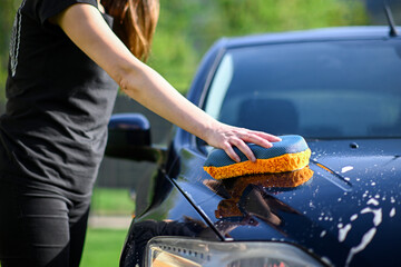 A young woman washes the car using an orange-gray sponge. a detailed view of the lights and a...