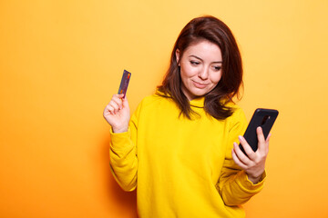 Portrait of caucasian lady gripping credit card to make purchase online with smartphone. Positive woman using internet banking and money to do shopping payment on mobile device.