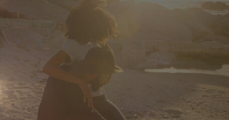 African American young adult and biracial young adult sitting on beach at sunset