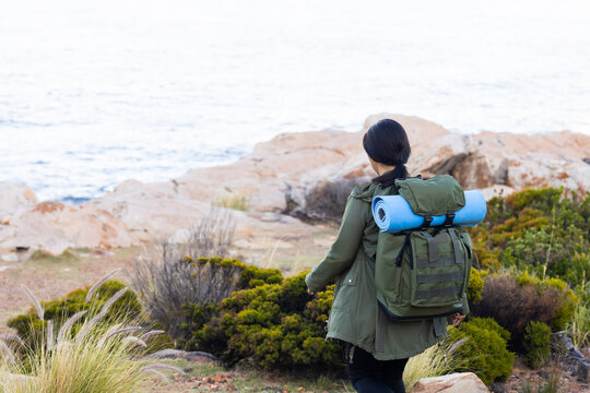 Biracial female hiker walking near the sea, surrounded by the serene beauty of nature, copy space