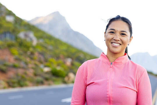 Biracial female hiker standing on mountain road, smiling, with copy space