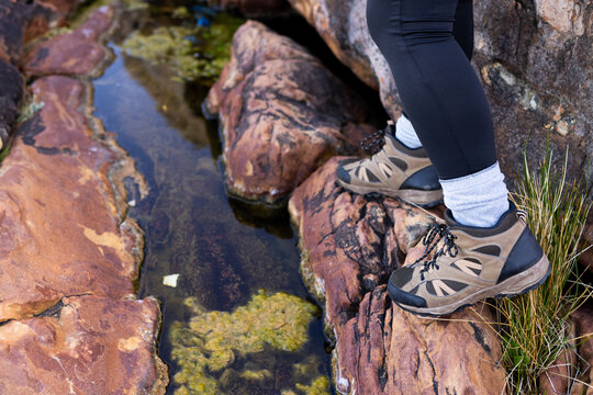 Biracial female hiker stepping on rocks by a stream, surrounded by lush greenery and the serene soun