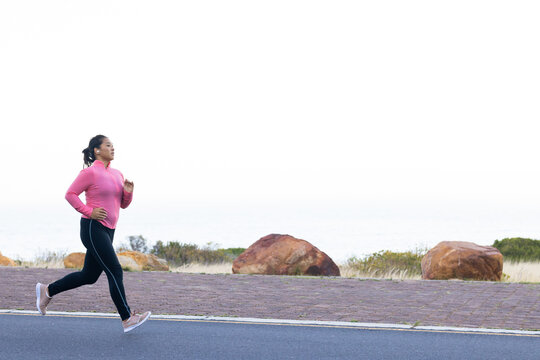 A biracial female hiker is jogging by the seaside, surrounded by the serene beauty of nature, copy s