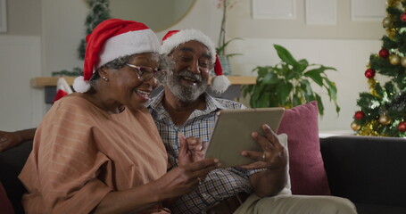 Senior biracial couple wearing Santa hats looking at tablet