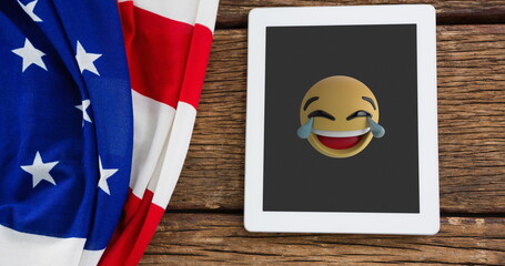 Naklejka premium A digital tablet displaying laughing emoji rests on a wooden surface