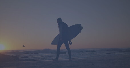 Fototapeta premium Caucasian young adult walking on beach, holding surfboard
