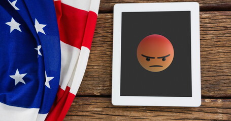 A tablet displaying angry emoji rests beside an American flag