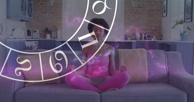African American yoga practitioner sitting cross-legged on couch, meditating