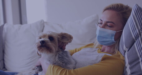 Caucasian woman wearing mask cuddling with a dog on a couch