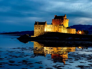 Eilean Donan Castle at night illuminated on an island with glowing windows at night