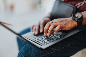 Close-up of a businessperson's hands typing on a laptop keyboard, conducting work remotely in an urban outdoor setting.