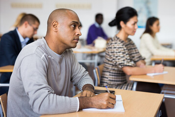 Focused adult latin american man listening to lecture in classroom with group. Postgraduate...