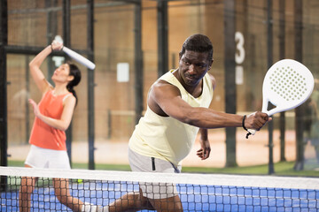 African male player ready to hits the ball while playing padel on a hard court
