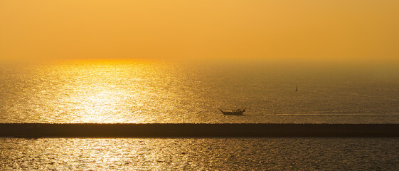 Panorama of the sea at dawn, sunrise, morning, a small boat sailing along the long pier, Manama,...