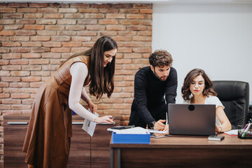 Three professionals collaborating at a desk with laptop in a modern office setting, depicting teamwork and focus.