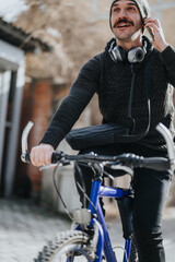 An urban male cyclist with a beanie and headphones pauses during a leisurely bike ride in the city.